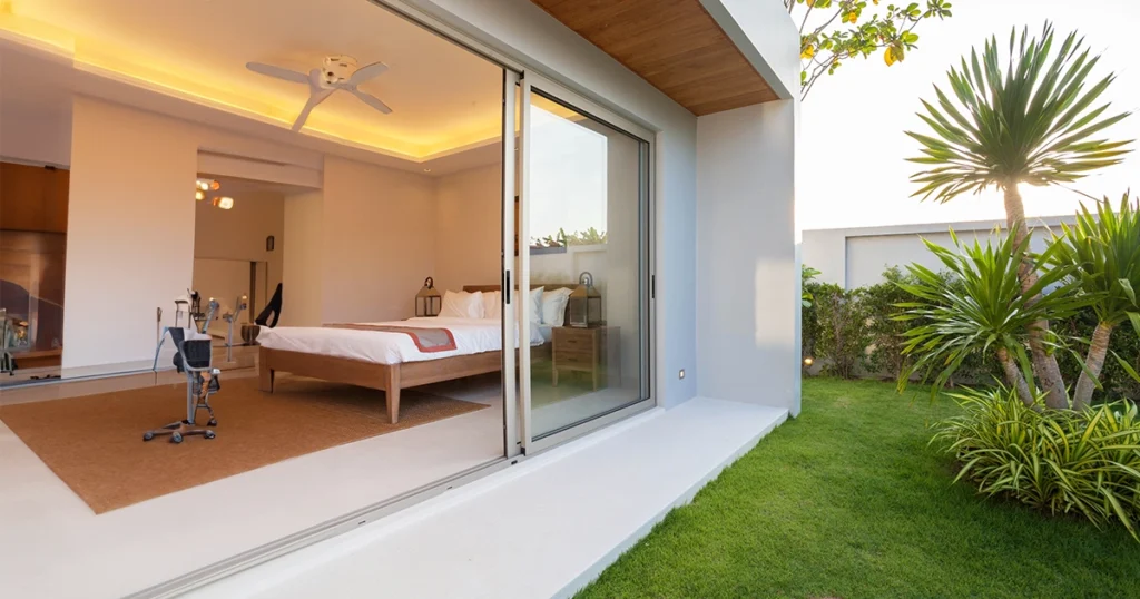 Modern bedroom with a large sliding uPVC window opening into a landscaped garden, showcasing natural light, energy efficiency and a seamless indoor-outdoor experience.