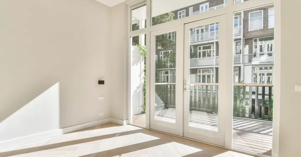 A bright modern room featuring large glass uPVC doors with sleek uPVC door handles opening to a balcony overlooking residential buildings.

