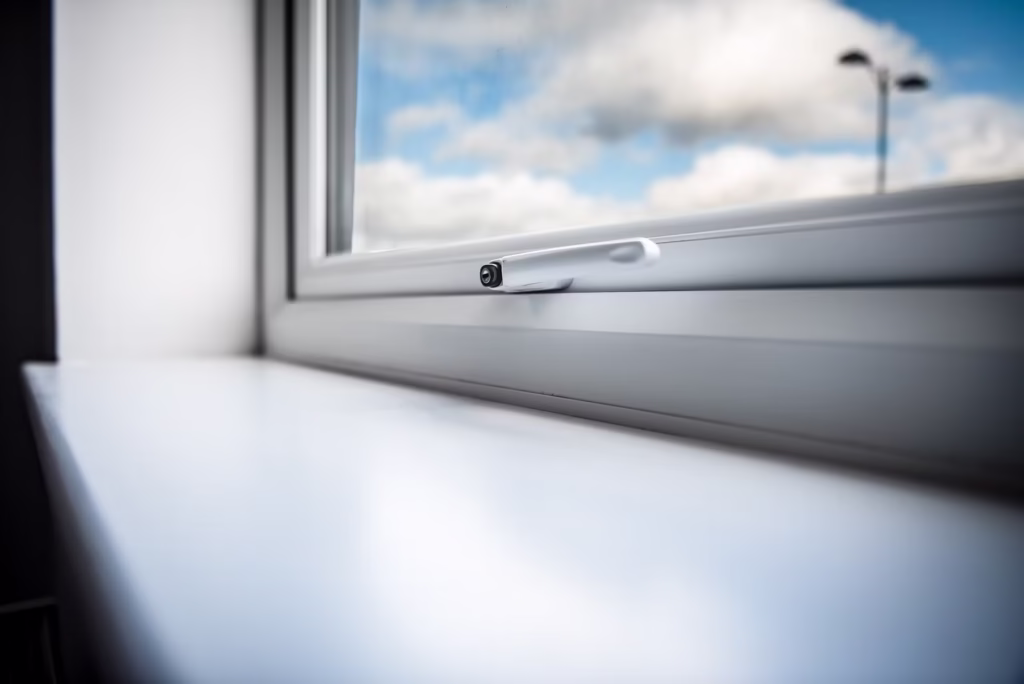 A sleek white uPVC window latch designed to match modern uPVC door handles, shown in a bright luxury interior with clear outdoor views.
