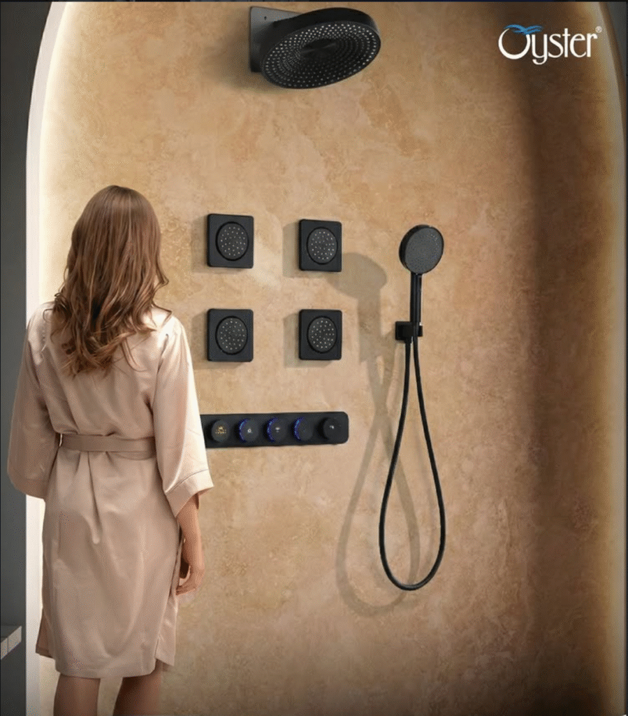 Luxury wall-mounted multi-jet shower system by Oyster Lifestyle featuring multiple square body jets, overhead rain shower, handheld shower, and illuminated control knobs installed on textured beige bathroom wall.